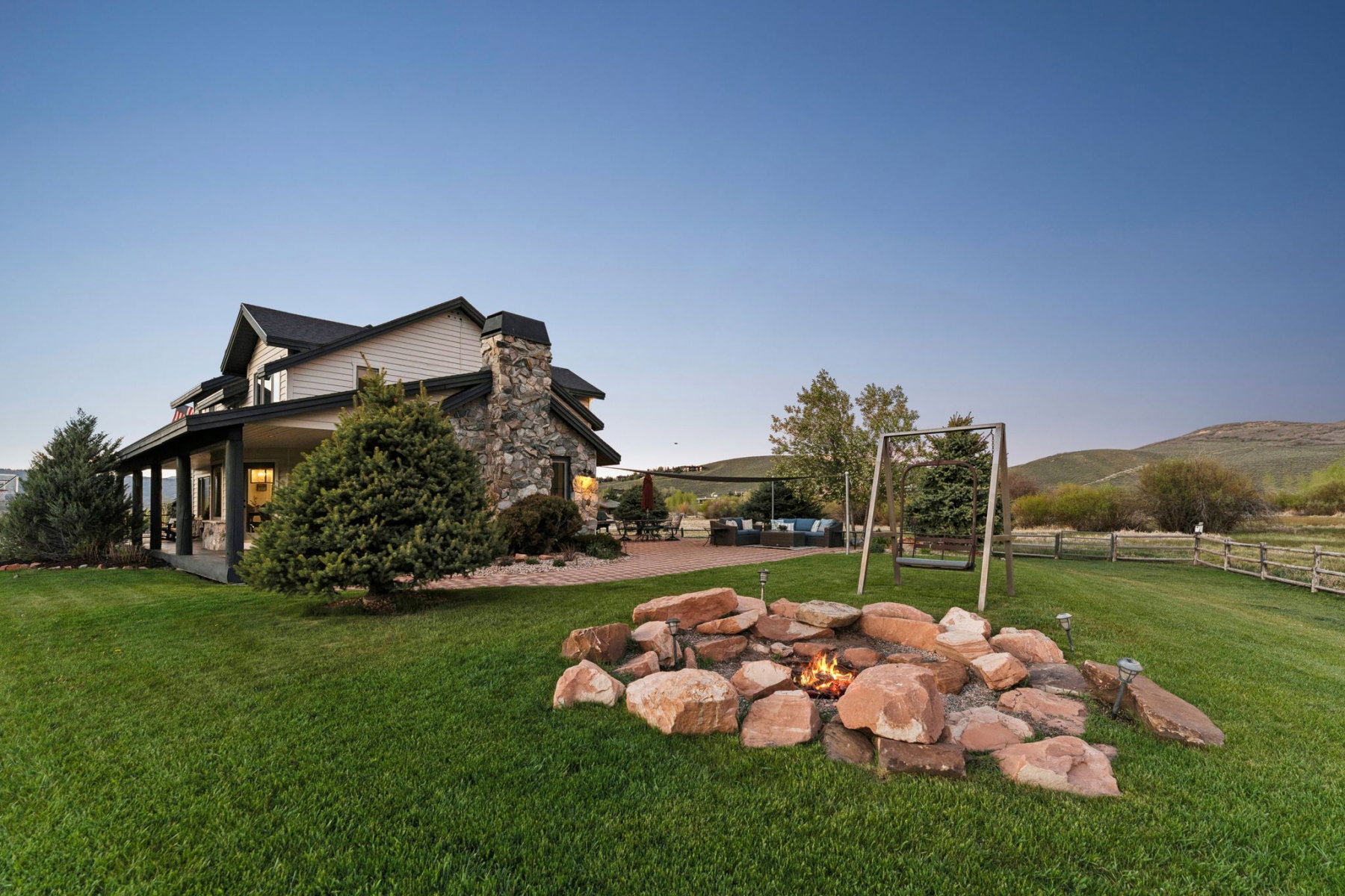Expansive backyard featuring a natural stone fire pit, swing set, and manicured lawn