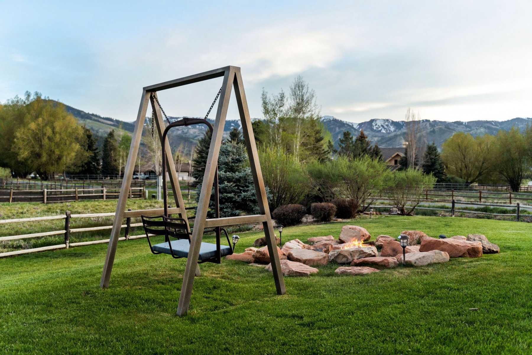 Expansive green lawn featuring a wooden swing set and a stone fire pit
