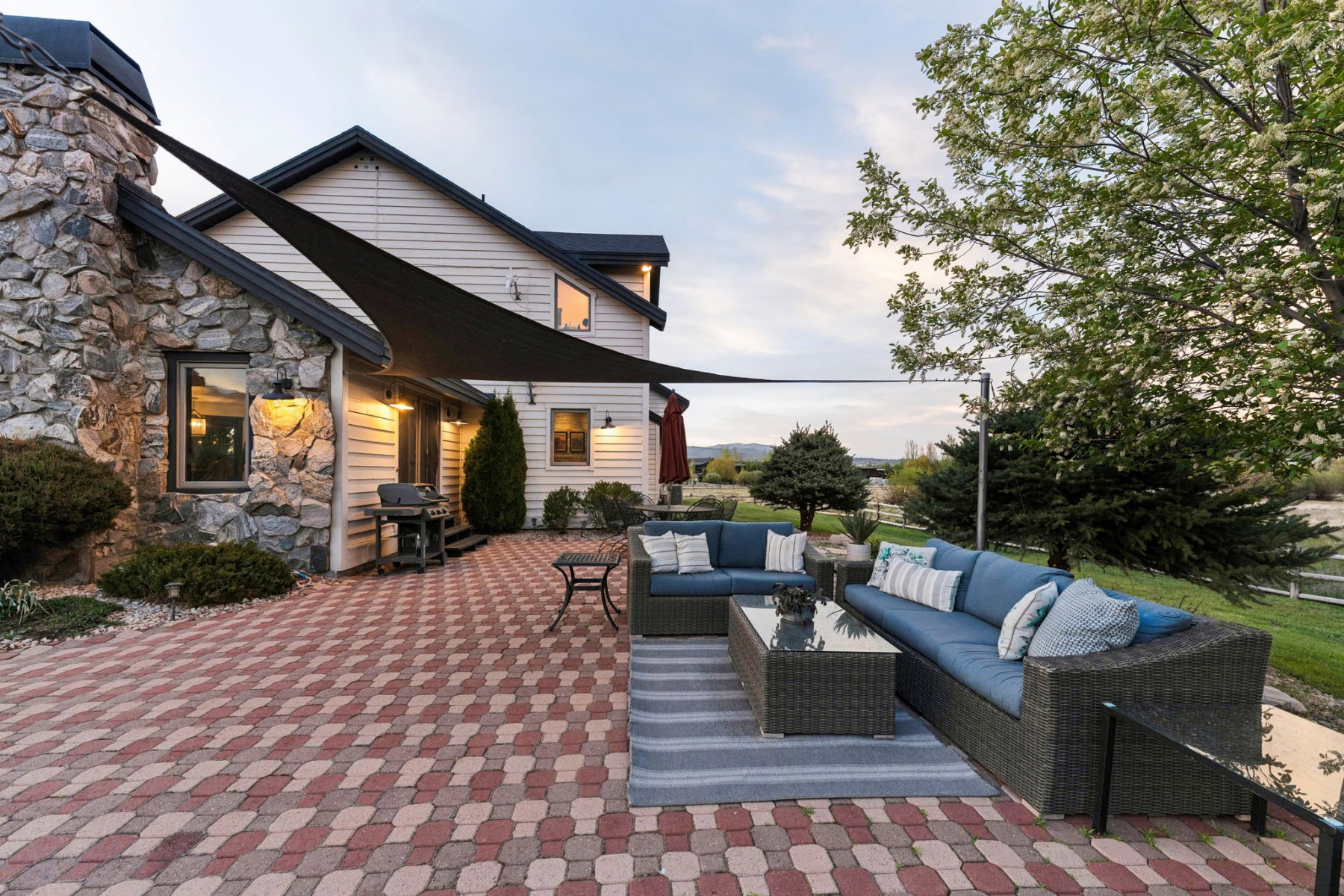 Expansive paver patio featuring a stone-clad exterior, white siding, and a shade sail