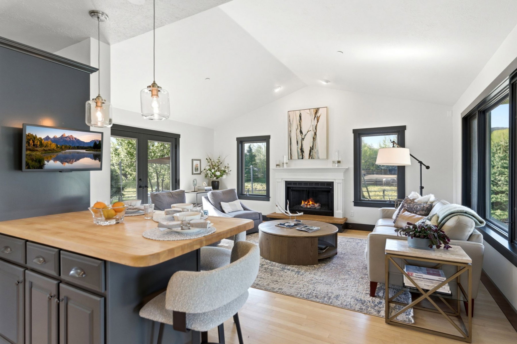 Open-concept living area featuring vaulted ceilings, a central fireplace with a white mantel, and wood-finish flooring