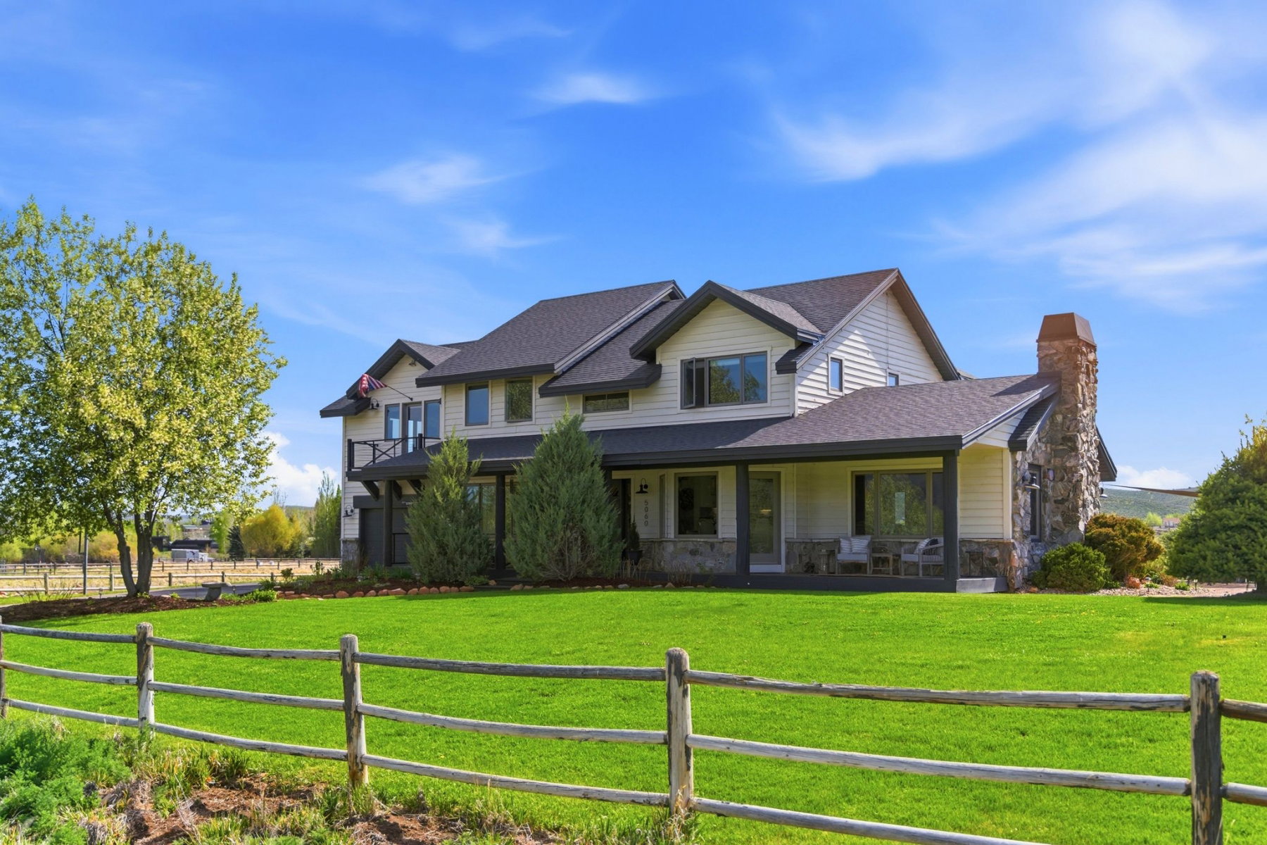 Two-story property with light-toned siding, dark trim, and a prominent stone-clad chimney
