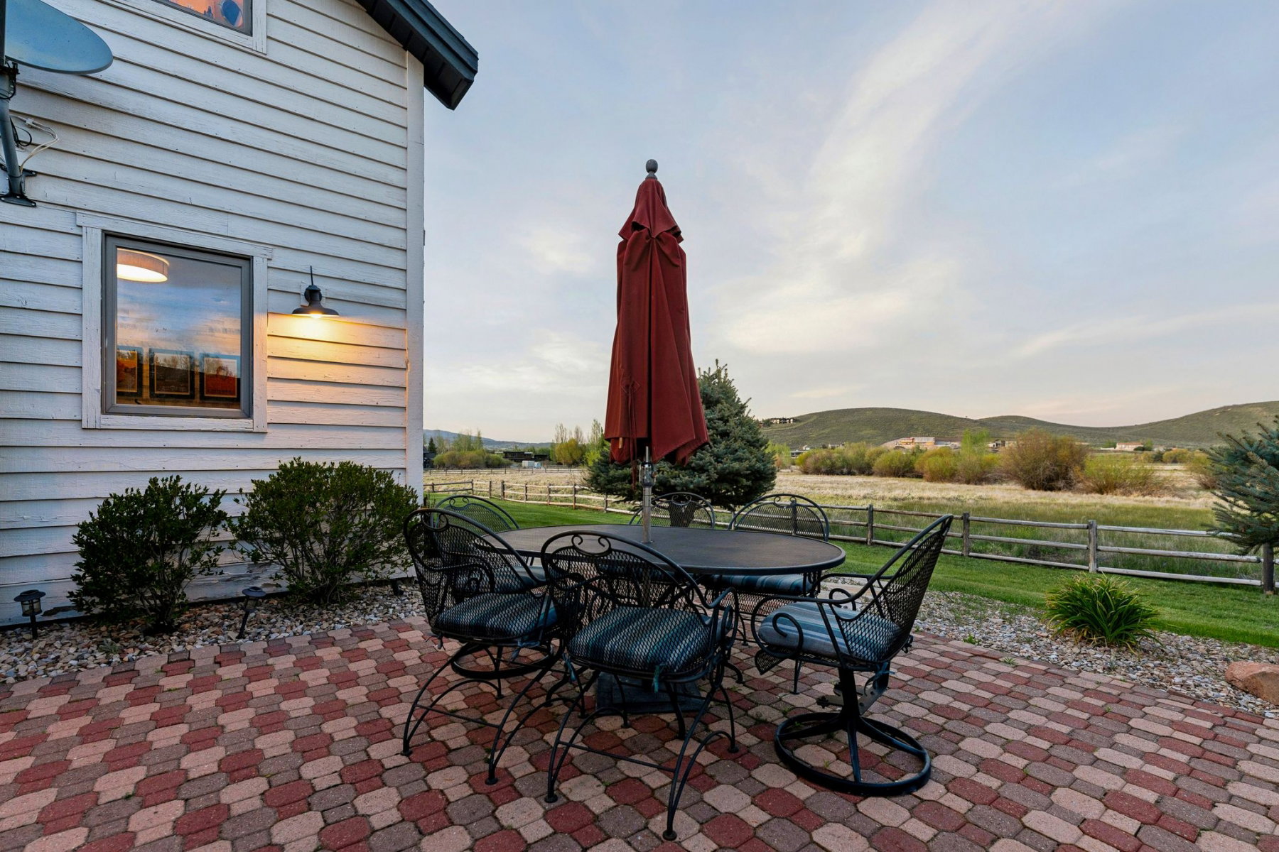 Brick paver patio featuring a rustic split-rail fence, distant rolling hills, and mature landscaping