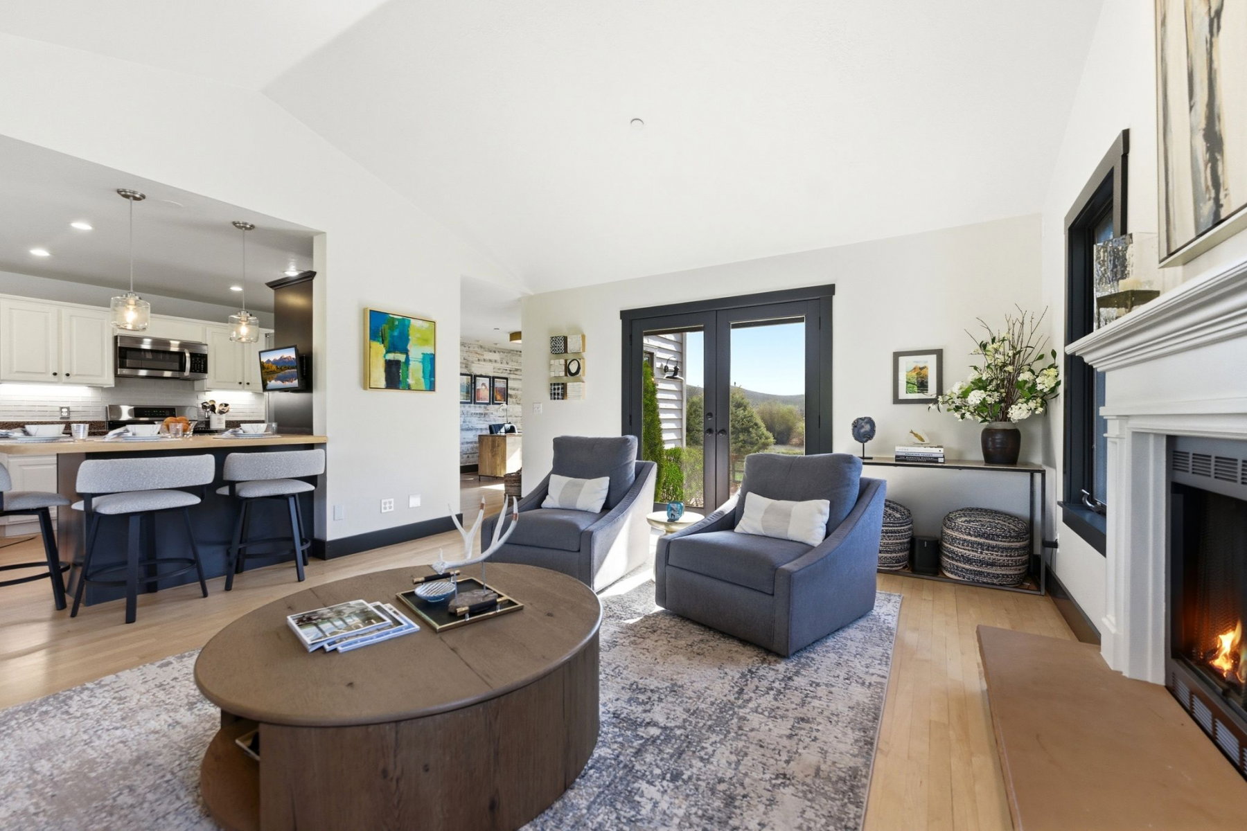 Open-concept living area featuring a fireplace with a white mantel, light wood-finish flooring, and white walls