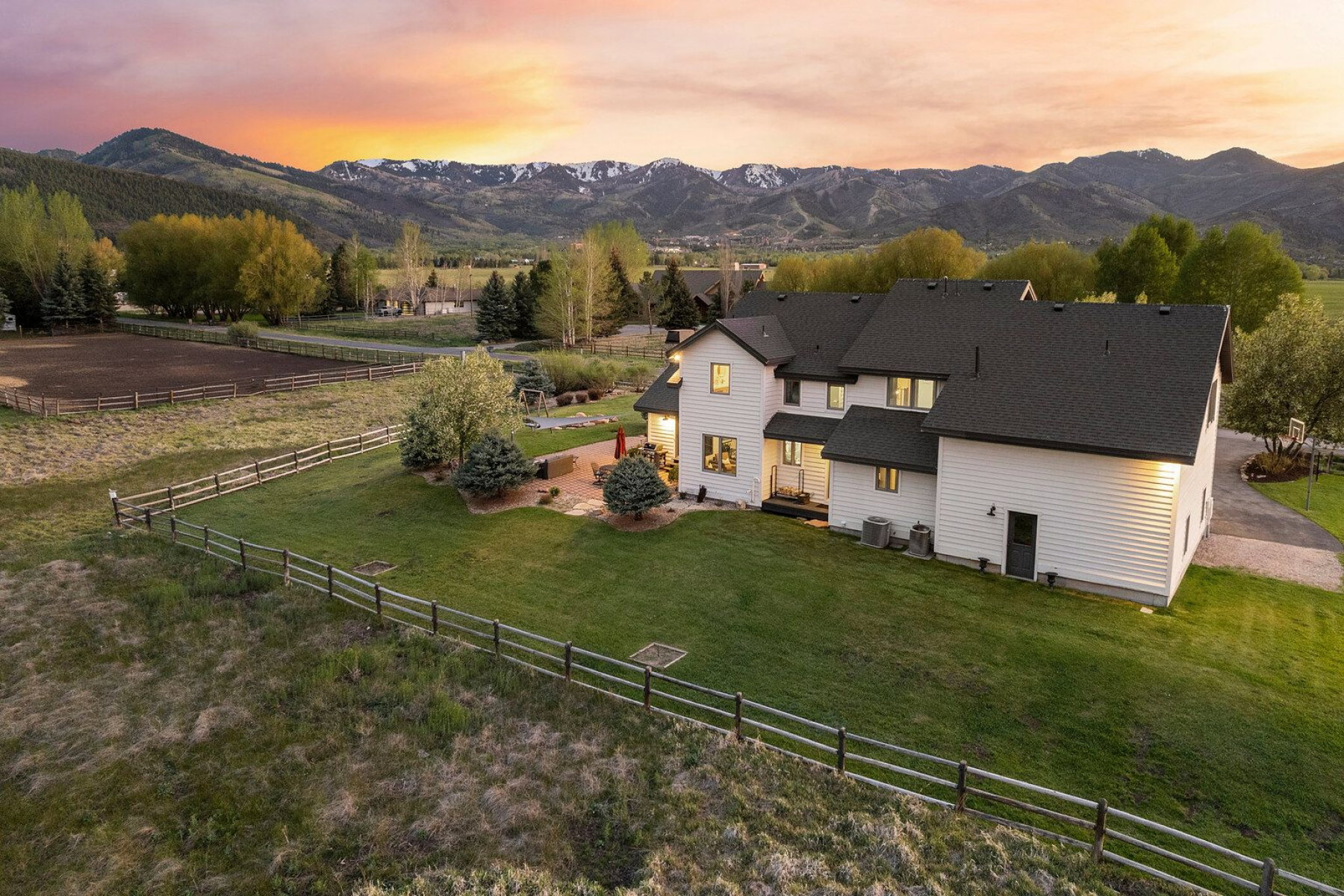 Expansive property featuring a white siding residence with a dark shingle roof, a manicured lawn, and a fenced pasture