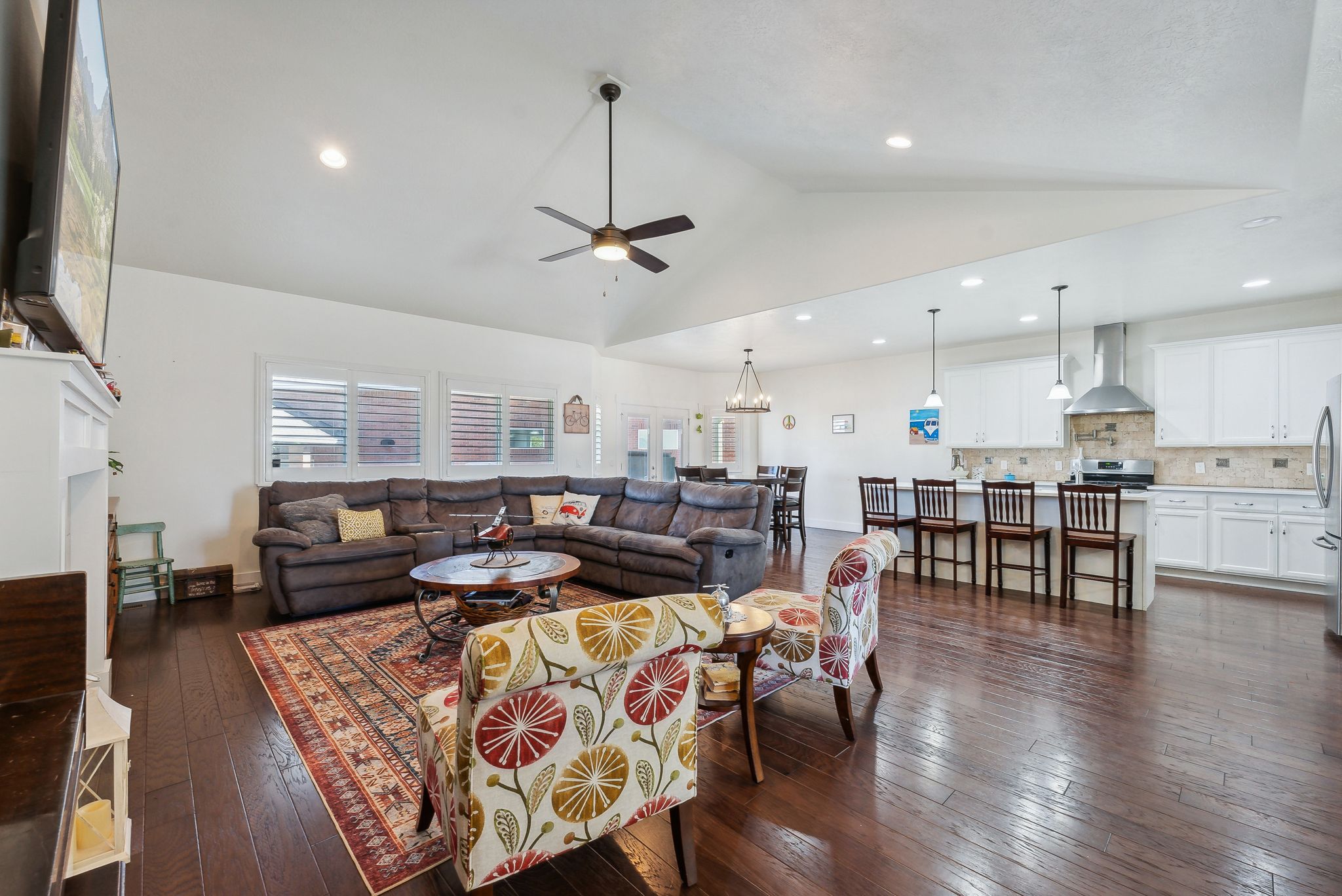 Spacious open-concept living area featuring wood-finish flooring, vaulted ceilings, and a ceiling fan