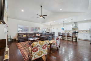 Spacious open-concept living area featuring wood-finish flooring, vaulted ceilings, and a ceiling fan