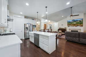Open-concept kitchen and living area featuring a central island with countertop seating, stainless steel appliances, white cabinetry, and wood-finish flooring