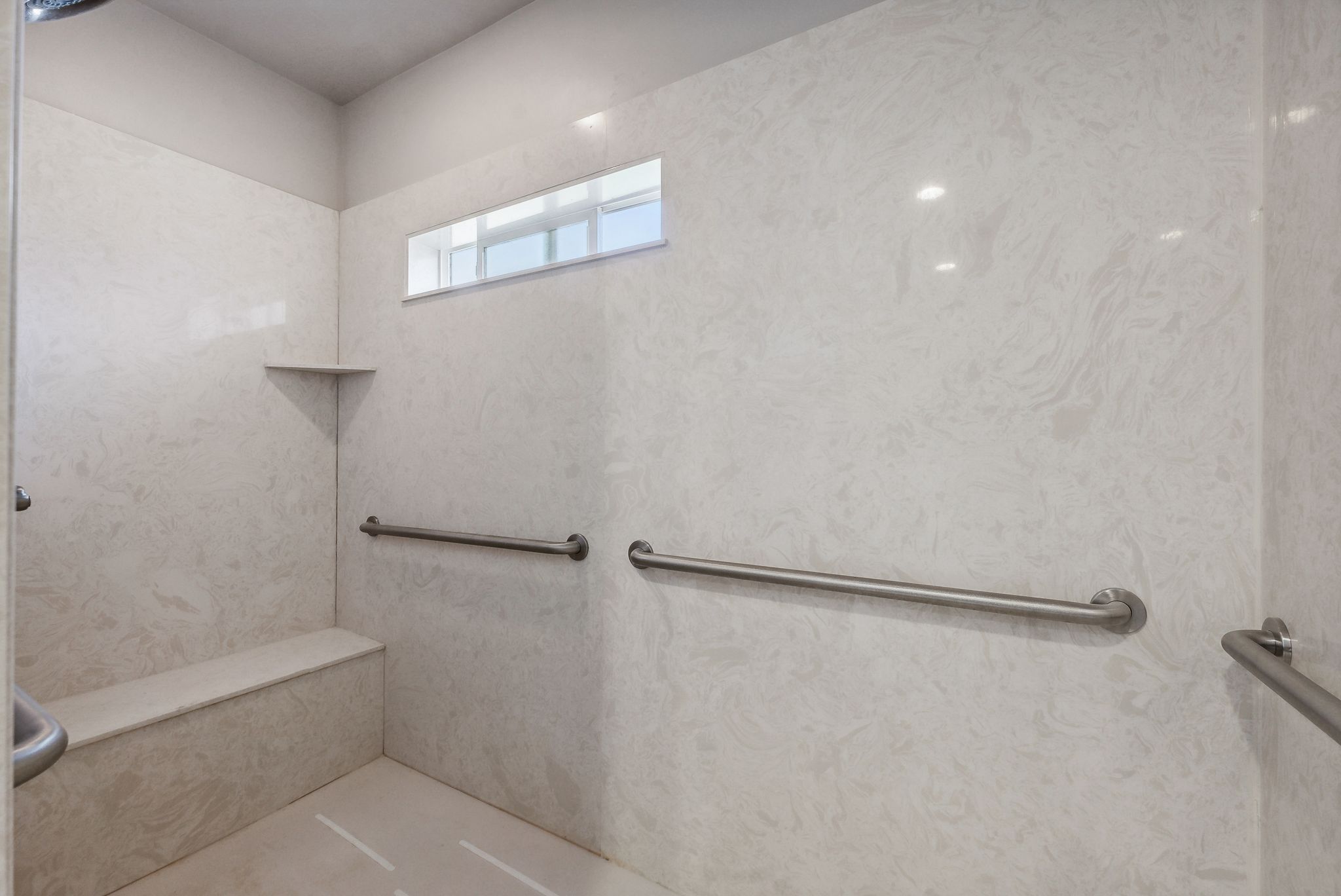 Expansive shower with light-toned wall panels, a built-in bench, and multiple grab bars