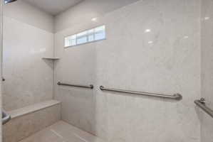Expansive shower with light-toned wall panels, a built-in bench, and multiple grab bars