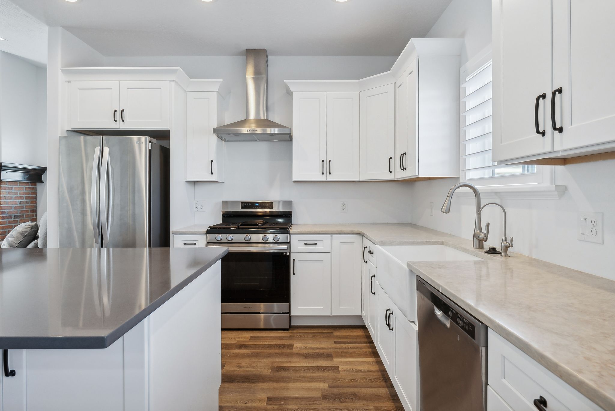 Custom built ADU/Modern kitchen featuring white shaker cabinetry, stainless steel appliances, wood-finish flooring, a farmhouse sink, and light-toned countertops