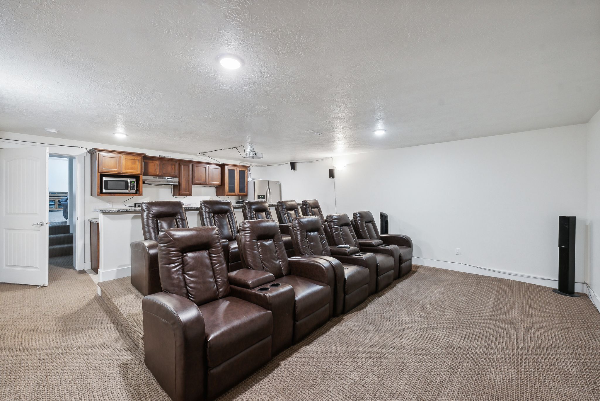 Theatre with full kitchen?Dedicated home theater room featuring tiered seating, recessed lighting, and a built-in wet bar with wood cabinetry and a stainless steel microwave