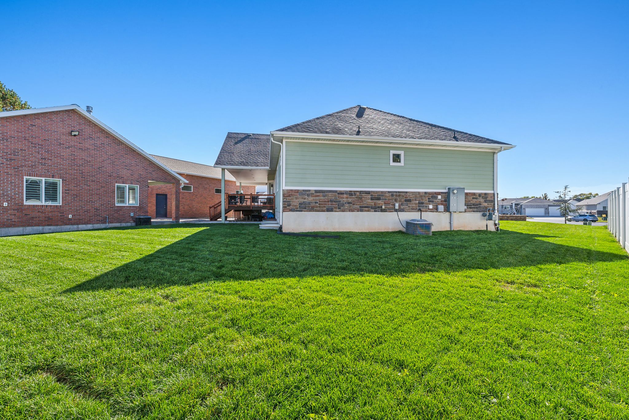 Expansive green lawn with a two-story residence featuring light green siding and a stone facade