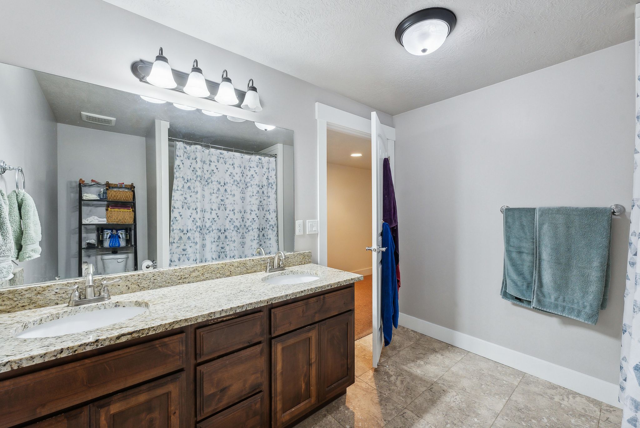 Bathroom featuring a dual vanity with light-colored speckled countertops, dark wood-finish cabinetry, and undermount sinks