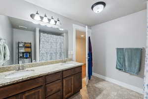 Bathroom featuring a dual vanity with light-colored speckled countertops, dark wood-finish cabinetry, and undermount sinks