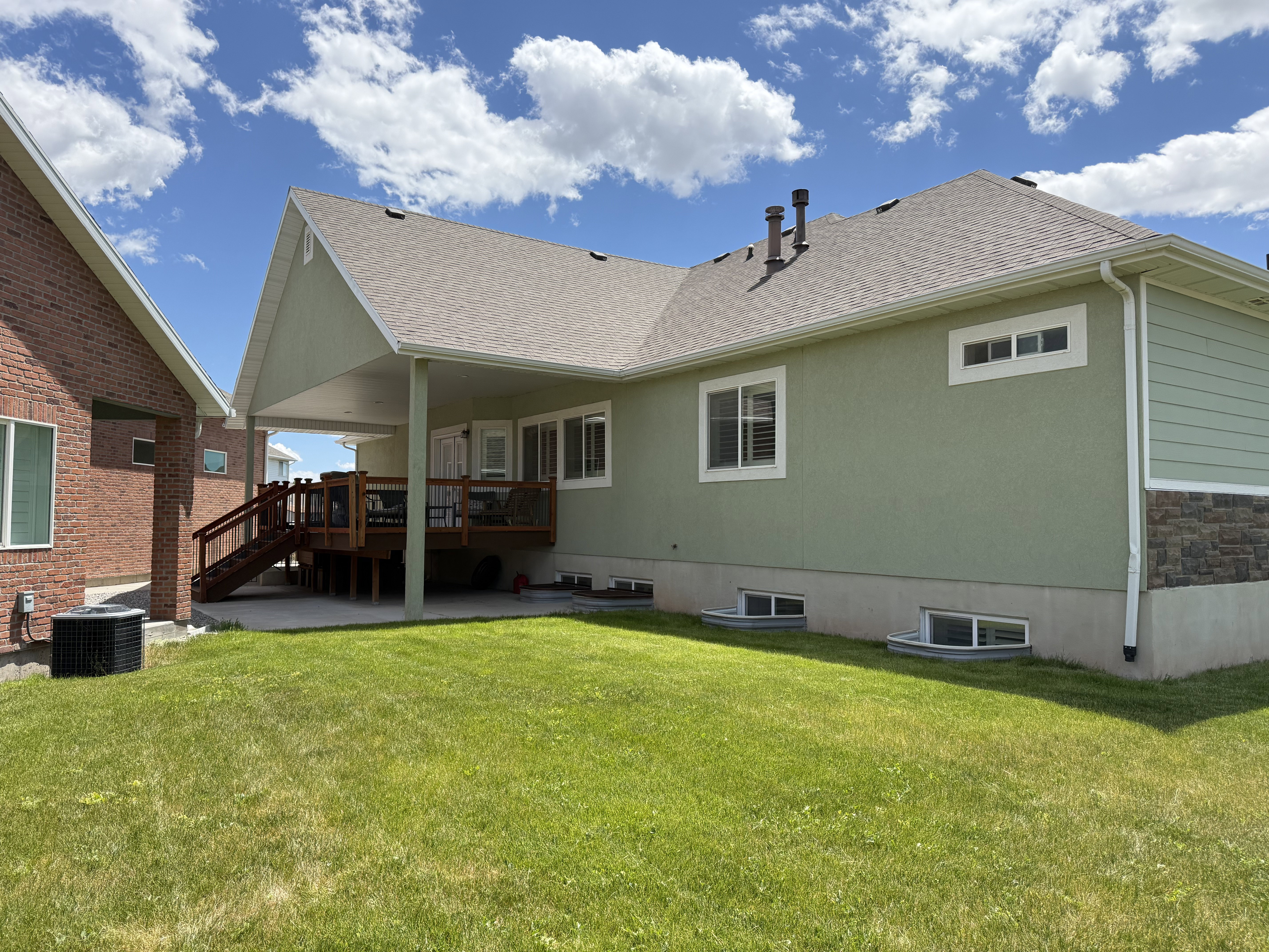 Expansive backyard featuring a covered deck with stained wood railing, a concrete patio, and a manicured lawn