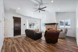 Custom built ADU/Spacious living area featuring wood-finish flooring, a brick fireplace with a dark wood mantel, and multiple windows with plantation shutters