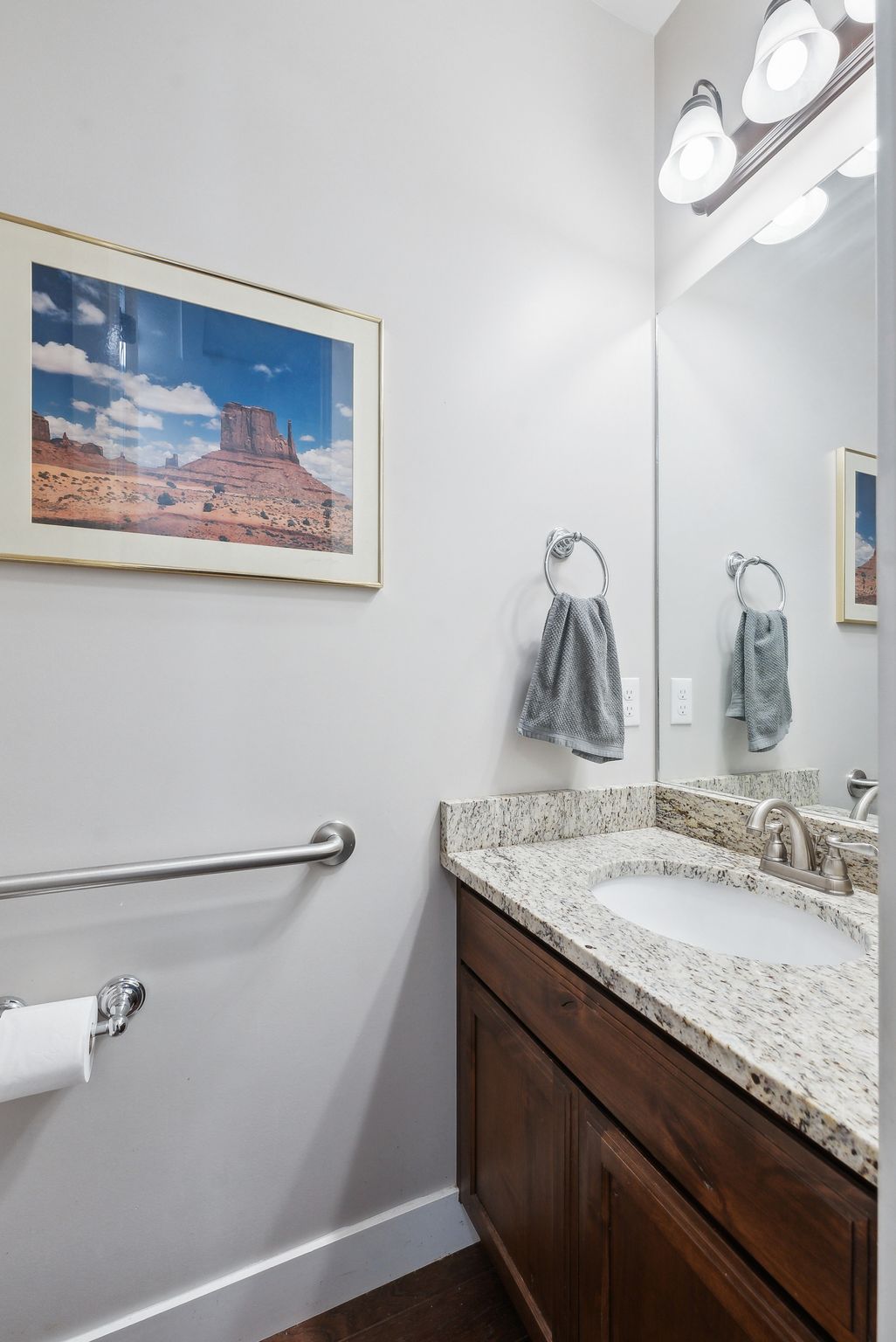 Powder room featuring a wood-finish vanity with an integrated sink, stone countertop, brushed nickel faucet, and overhead vanity lighting