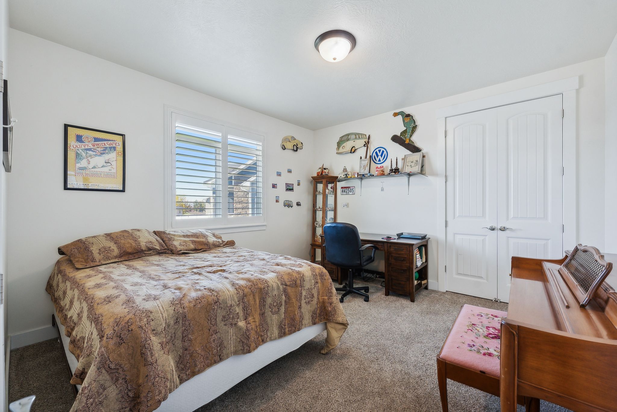 Bedroom/office Carpeted room featuring a double window with plantation shutters, a desk area with shelving, and a double-door closet with arched paneling