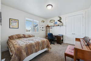 Bedroom/office Carpeted room featuring a double window with plantation shutters, a desk area with shelving, and a double-door closet with arched paneling