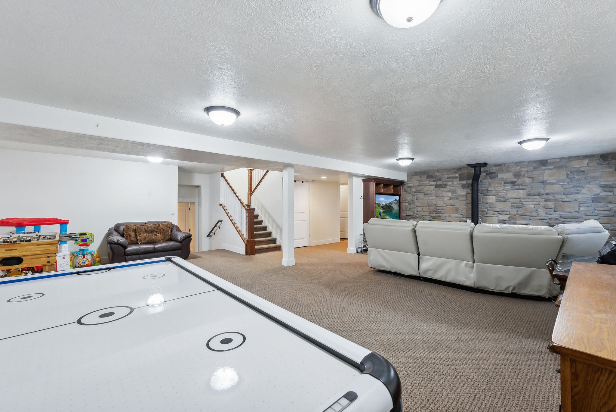 Finished basement space featuring carpeted flooring, a stone-accented wall, recessed lighting, and a built-in entertainment center