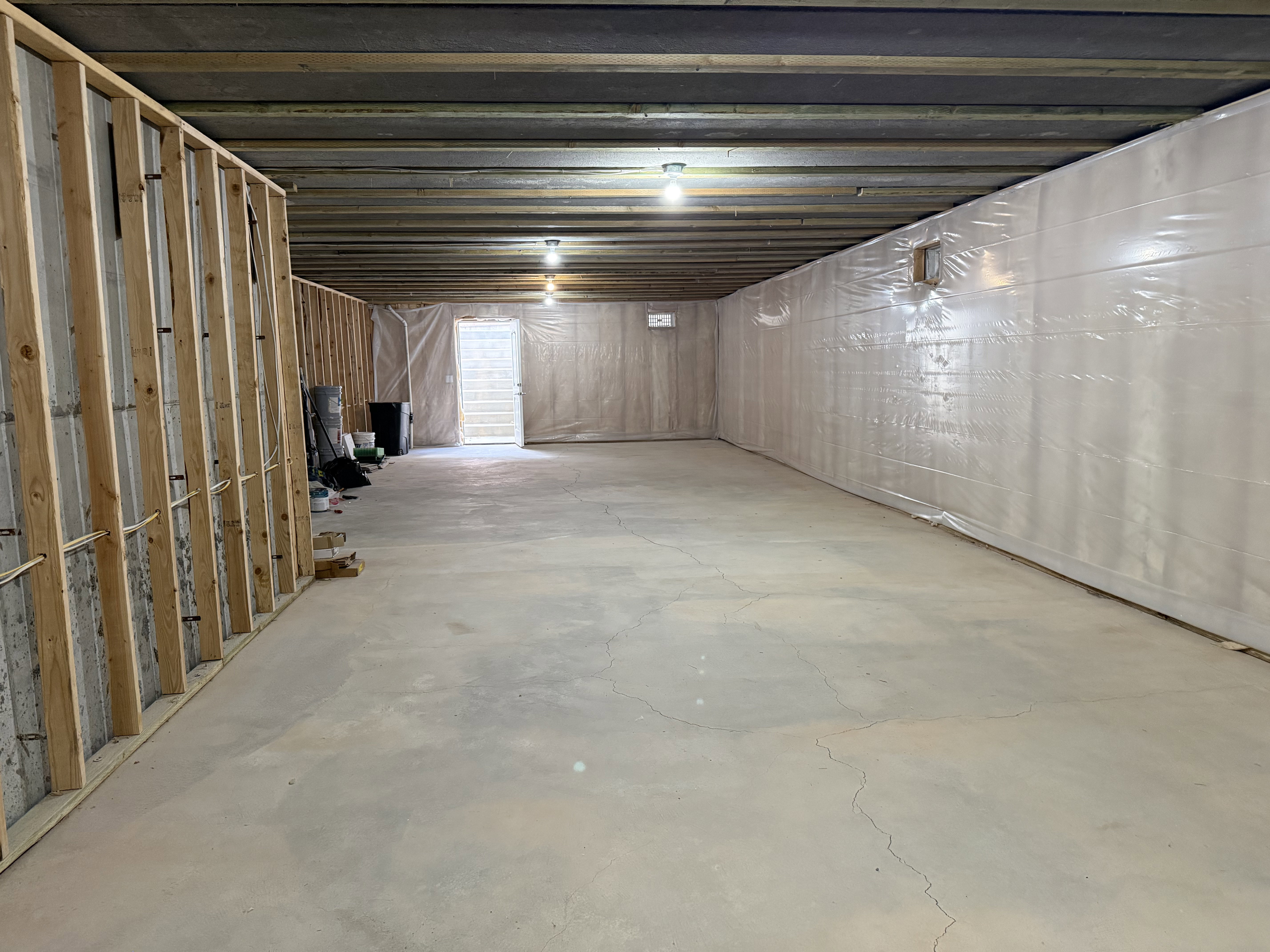 Expansive unfinished basement featuring concrete flooring, exposed ceiling joists, and a partial wood-framed wall