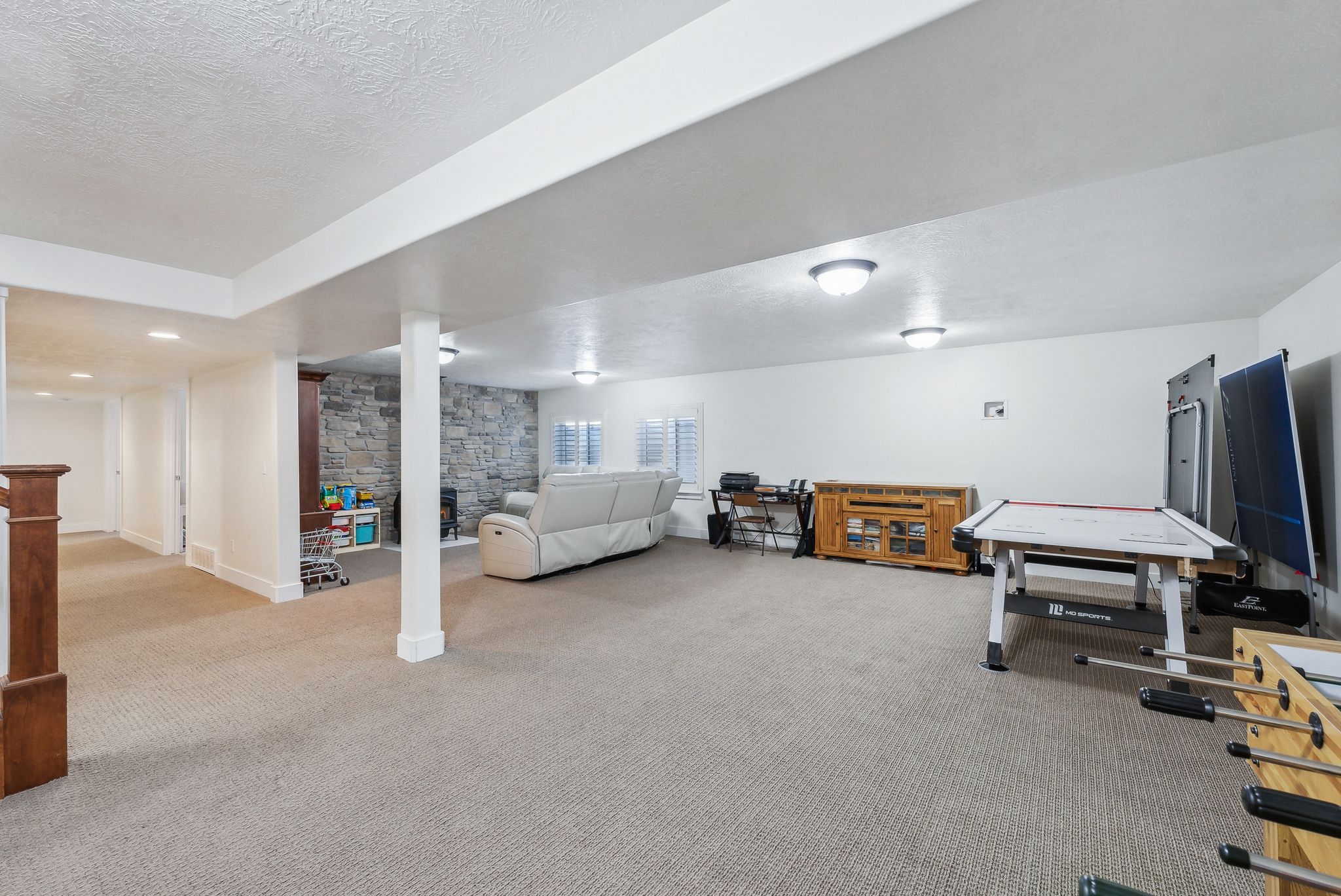 Expansive lower-level space featuring carpet flooring, recessed lighting, and a stone-clad fireplace