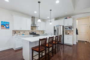 Spacious kitchen featuring an expansive central island with seating, white shaker-style cabinetry, stainless steel appliances, and wood-finish flooring