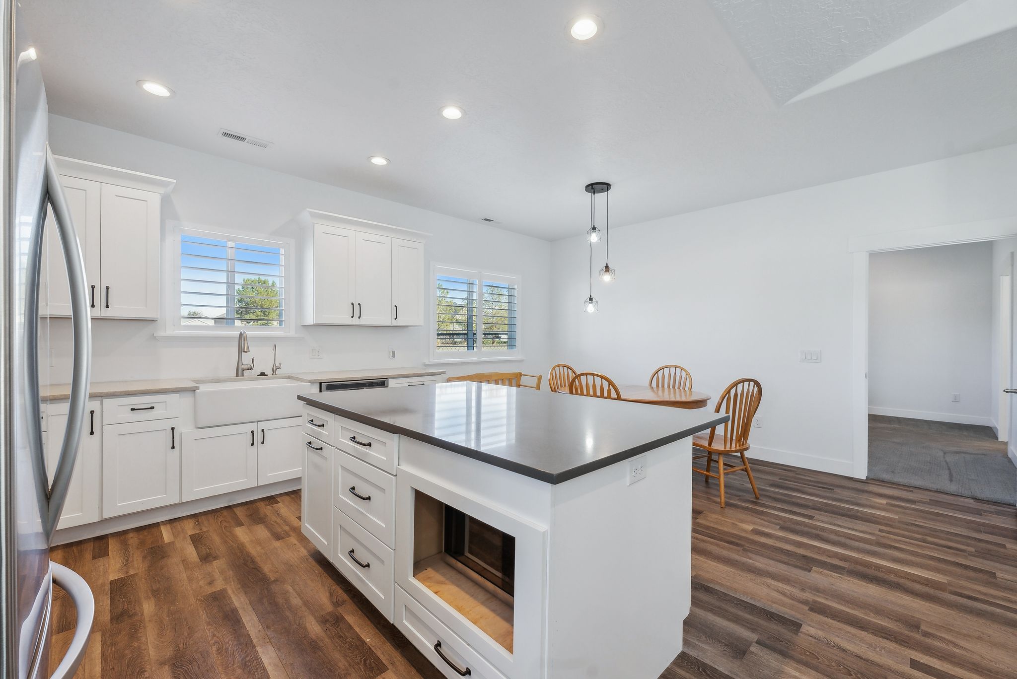 Custom built ADU/Modern kitchen featuring a central island with dark countertop, white cabinetry with black hardware, wood-finish flooring, a farmhouse sink, and recessed lighting