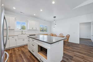 Custom built ADU/Modern kitchen featuring a central island with dark countertop, white cabinetry with black hardware, wood-finish flooring, a farmhouse sink, and recessed lighting