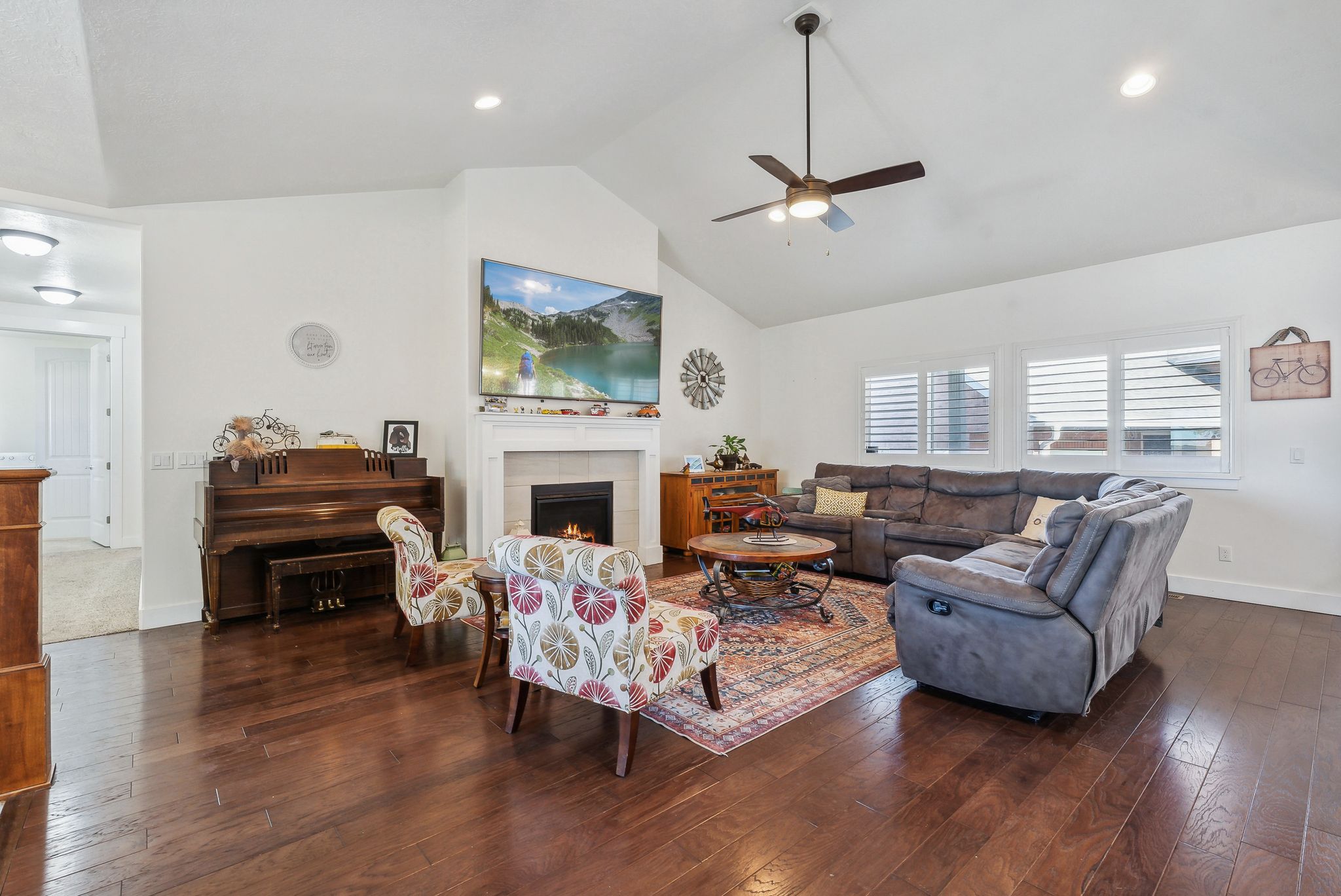 Spacious living area featuring vaulted ceilings with a ceiling fan, dark wood-finish flooring, and a white fireplace with a mantel