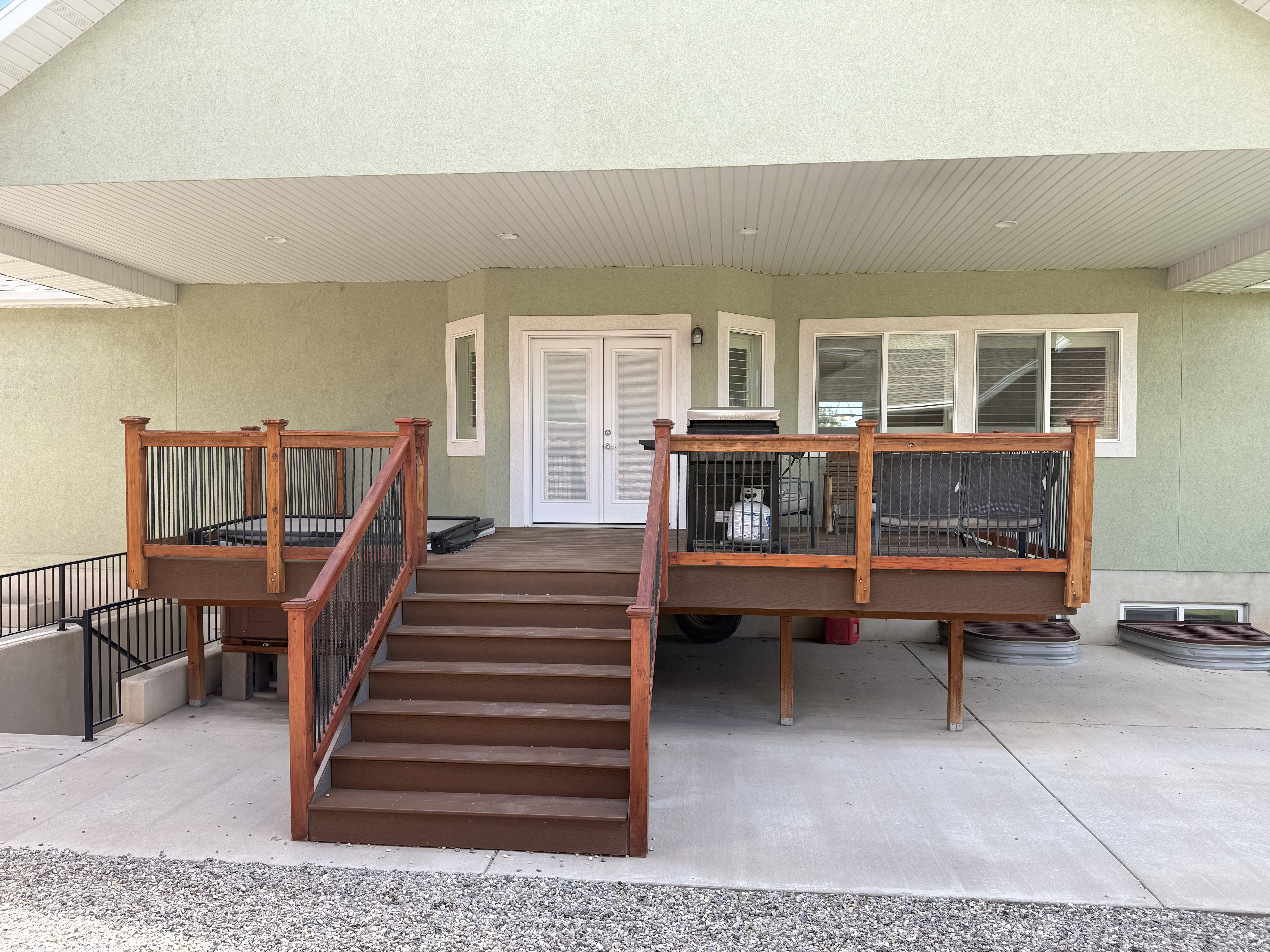 Lower-level deck featuring wood-finish railings with black balusters, providing access to the concrete patio