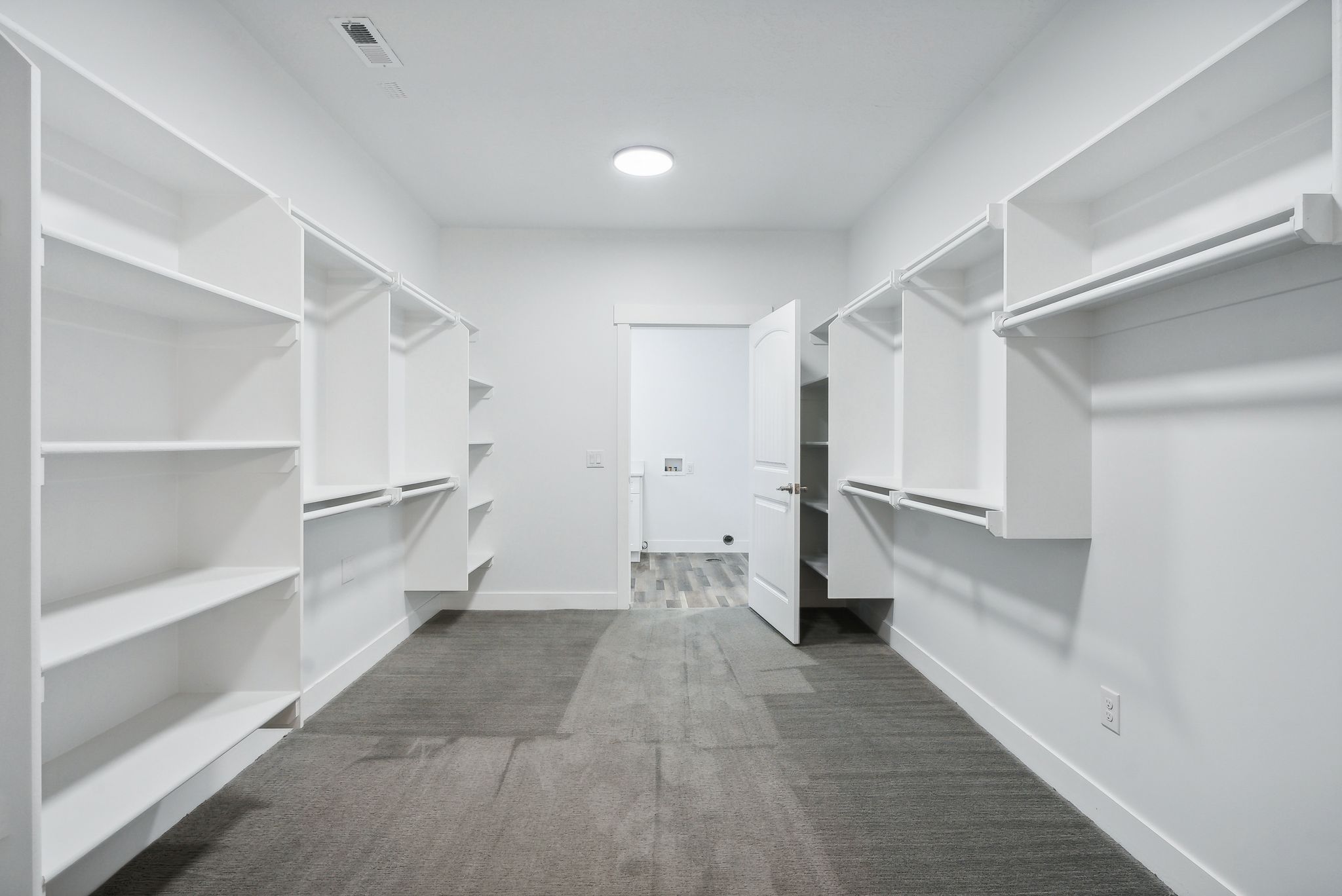 Custom built ADU/Spacious walk-in closet featuring extensive built-in shelving, hanging rods, and gray carpet flooring
