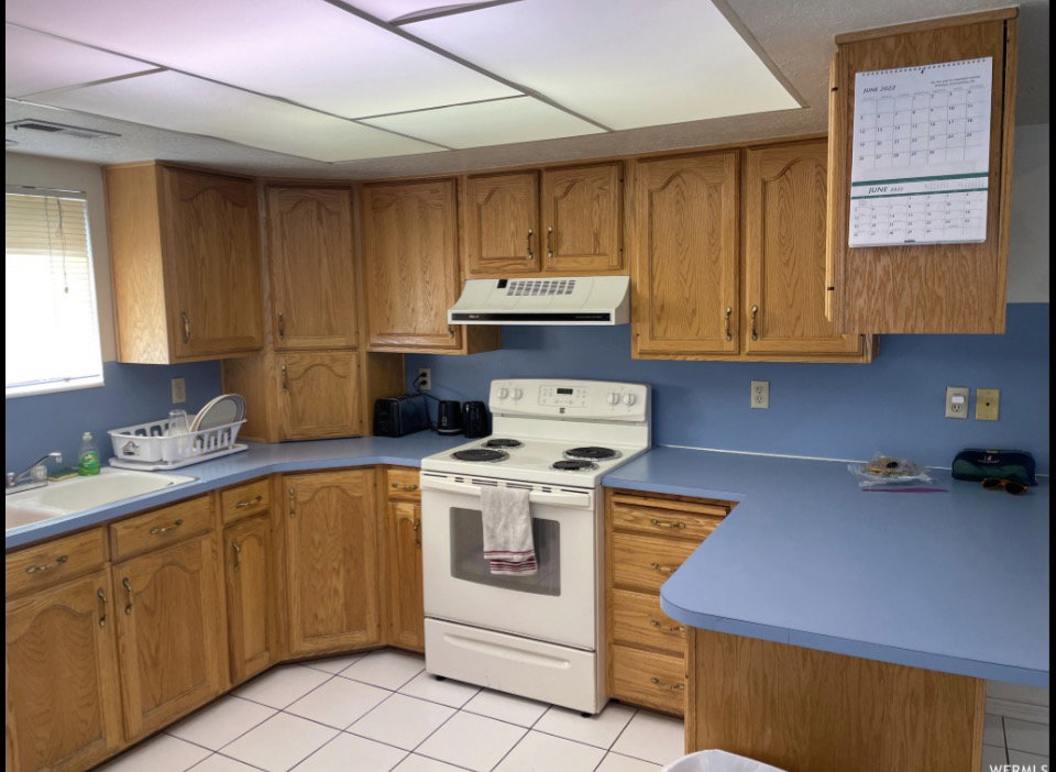Kitchen featuring extensive wood cabinetry, light blue countertops, a white range, and white square floor tiles