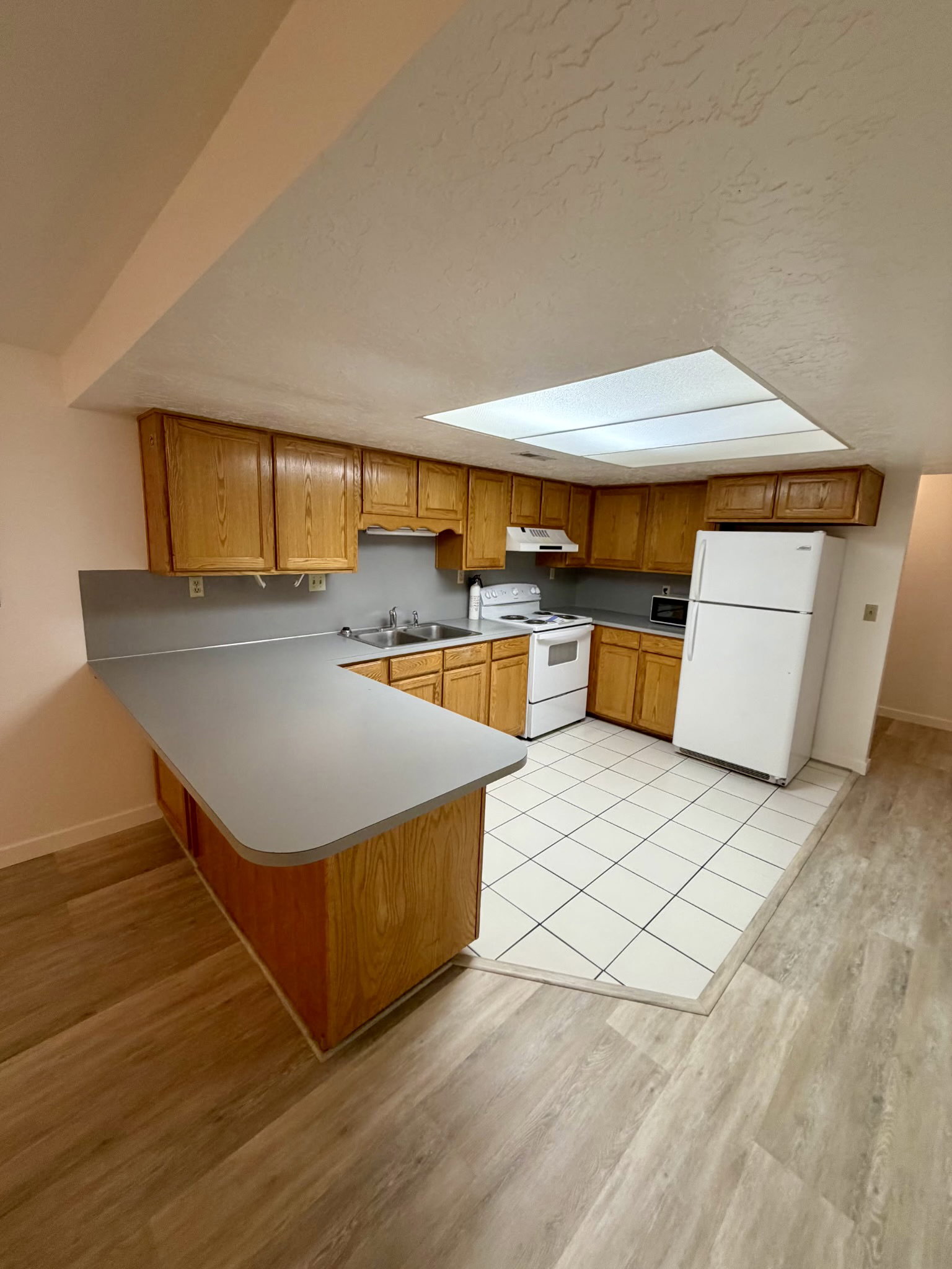 Kitchen featuring wood cabinetry, white appliances, a tile backsplash, and a breakfast bar