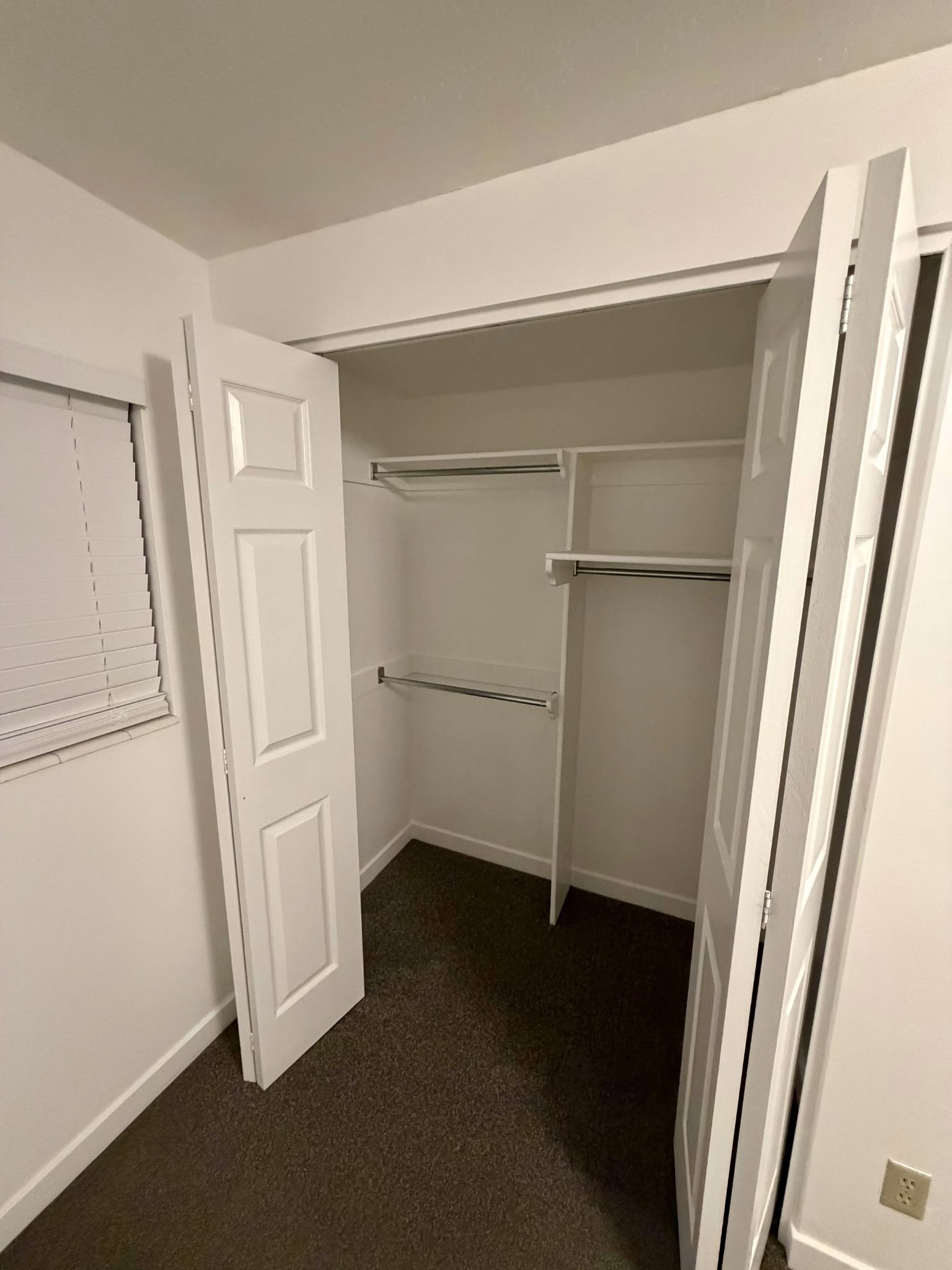 Spacious closet featuring bi-fold panel doors, upper and lower hanging rods, integrated shelving, and dark textured carpeting