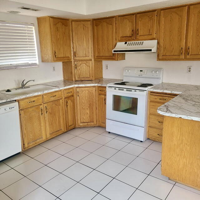Kitchen featuring wood cabinetry, white tiled flooring, patterned countertops, a built-in sink, and white appliances including a range and dishwasher