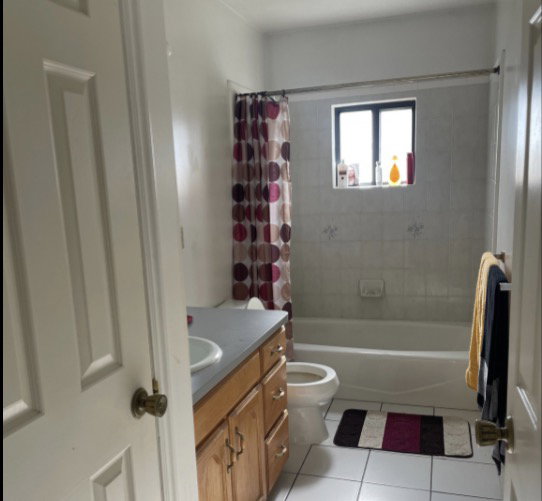 Bathroom featuring a built-in bathtub with tiled surround, a single window, and a vanity with a drop-in sink and wood-finish cabinetry