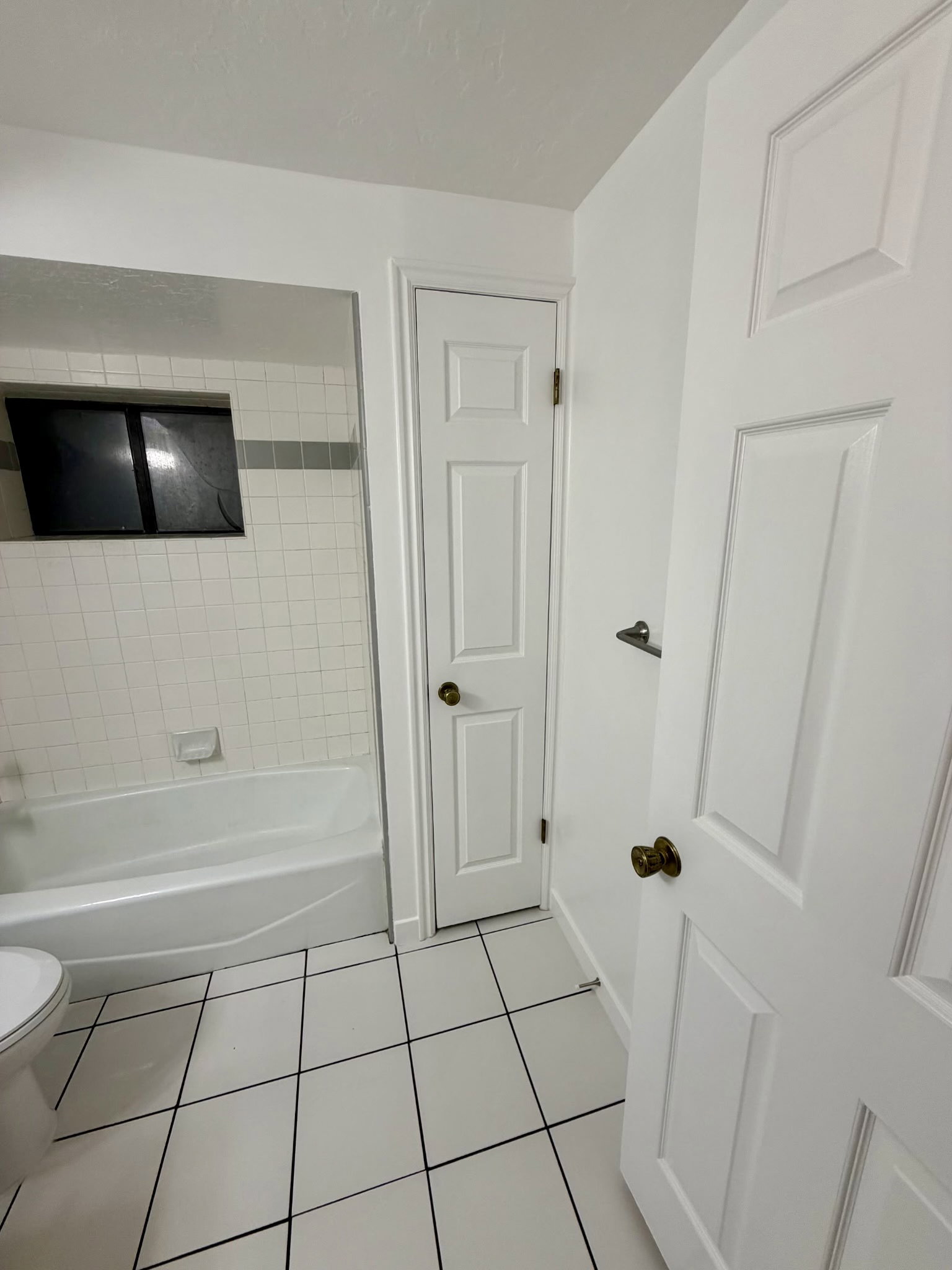 Bathroom featuring white subway tile with a gray accent stripe, a white bathtub, and white floor tiles with dark grout