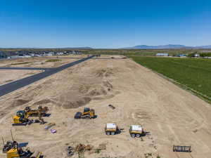 Expansive undeveloped land featuring a newly paved road, surrounding agricultural fields, and distant mountain ranges