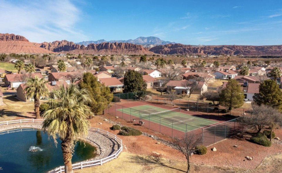 Community amenities featuring a tennis court, a pond with a fountain, and mature palm trees, all set against a distant mountain backdrop