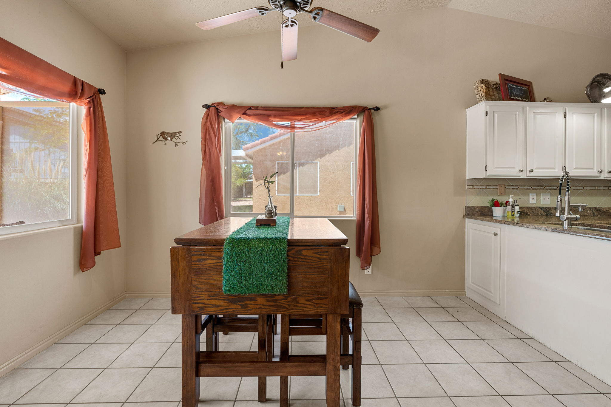 Vaulted ceiling with a ceiling fan, light-toned tile flooring, and two windows