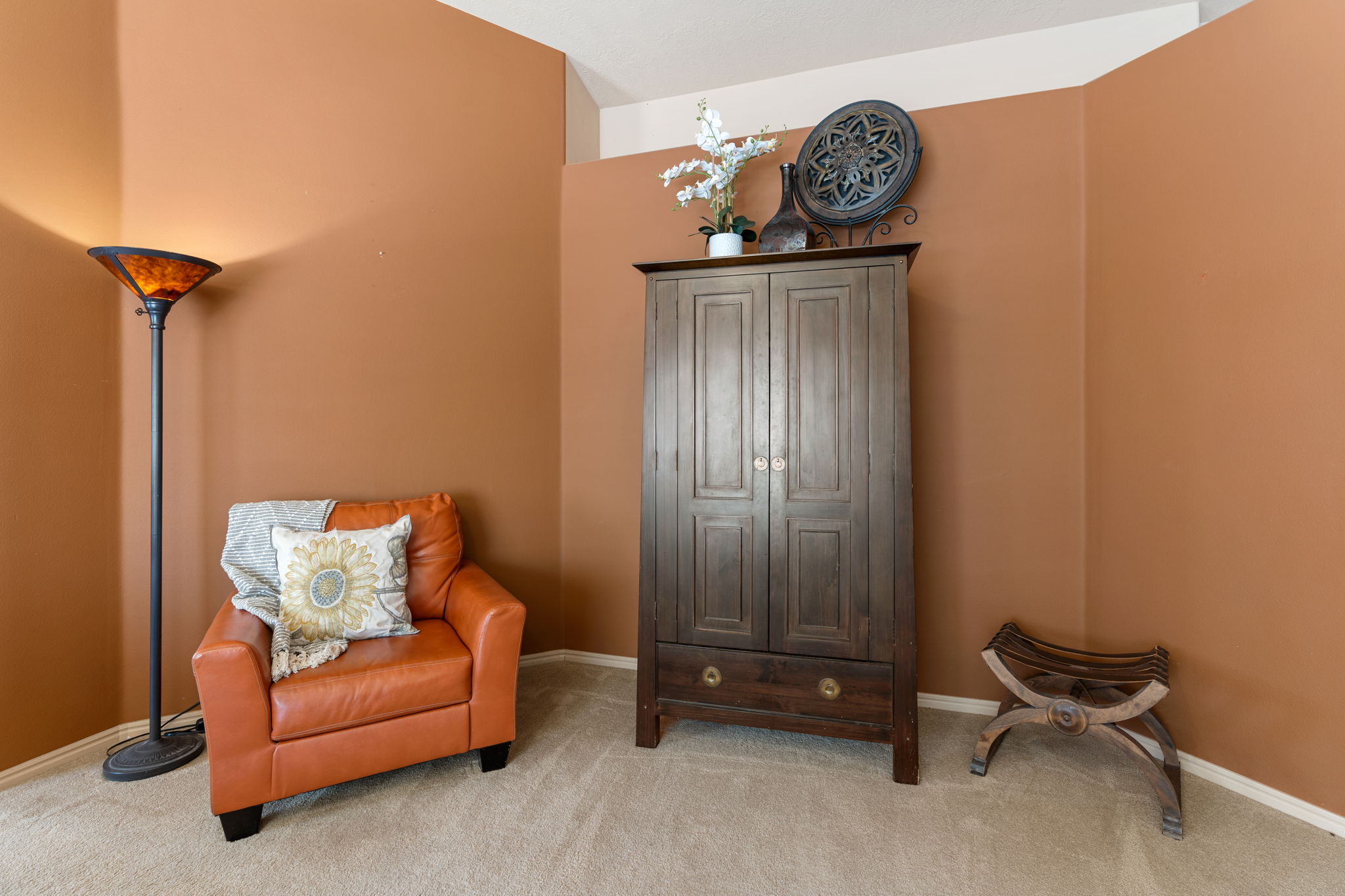 Carpeted room with a corner wall painted in a warm tone, featuring a white ceiling and baseboards