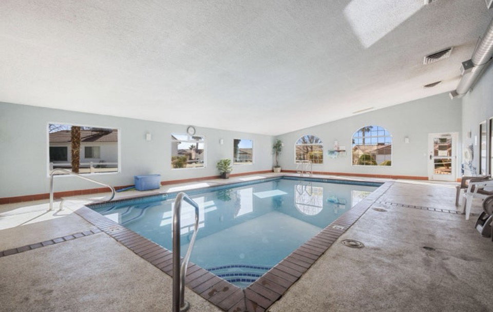Indoor swimming pool featuring a tiled perimeter and stainless steel handrails