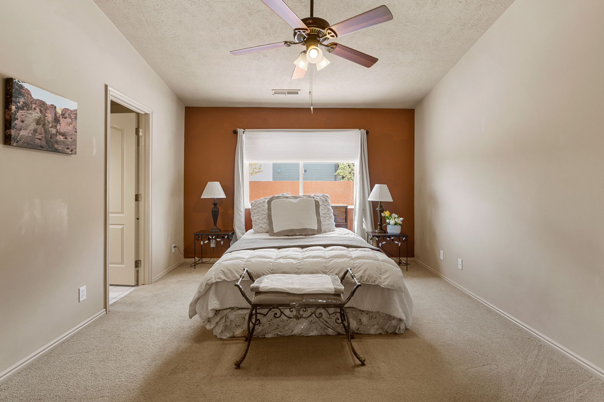 Carpeted room featuring a ceiling fan with integrated lighting, a window with a roller shade, and a contrasting accent wall