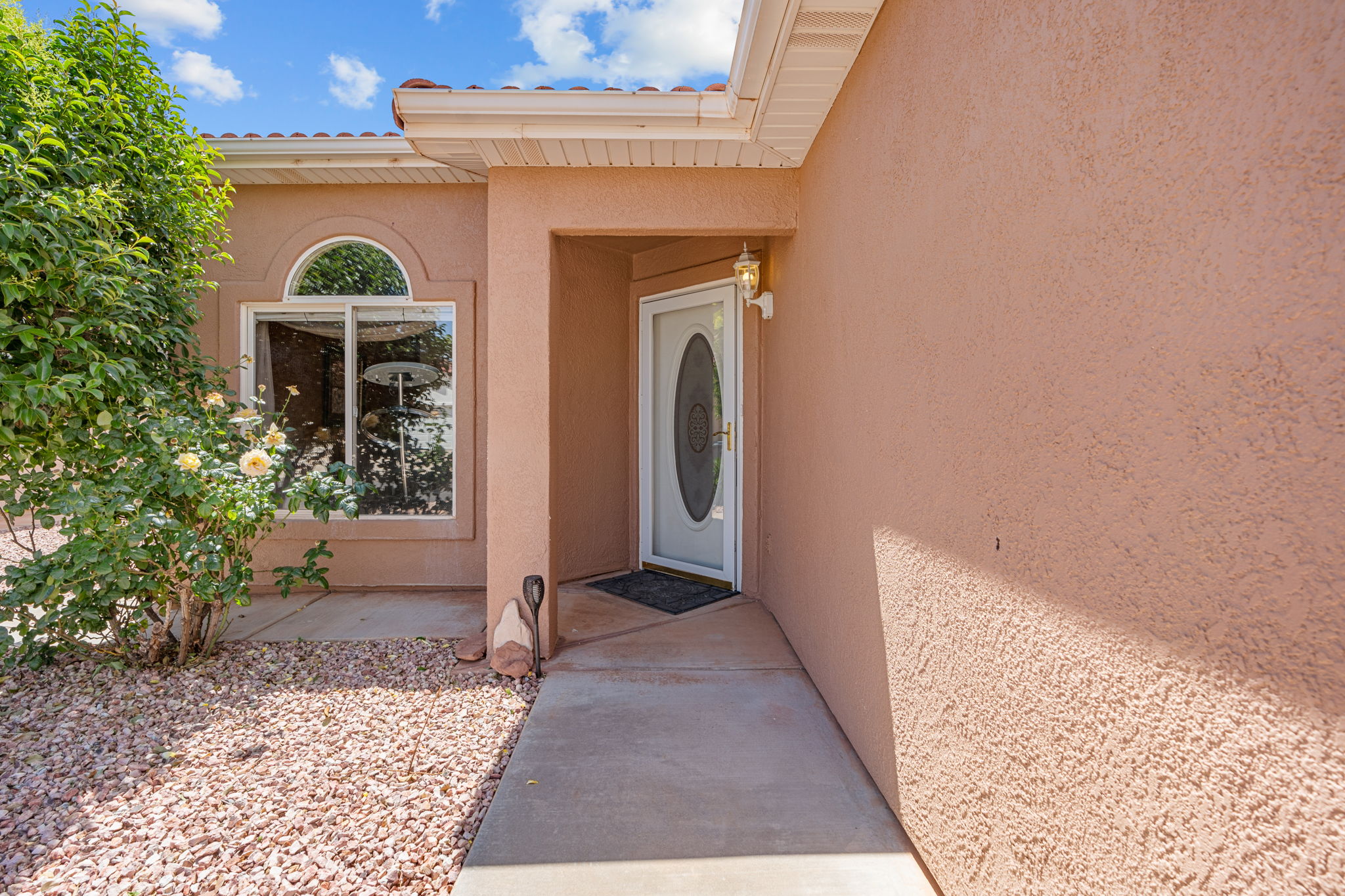 Stucco exterior with a tiled roof, featuring an arched window, white entry door with oval glass insert, and concrete walkway