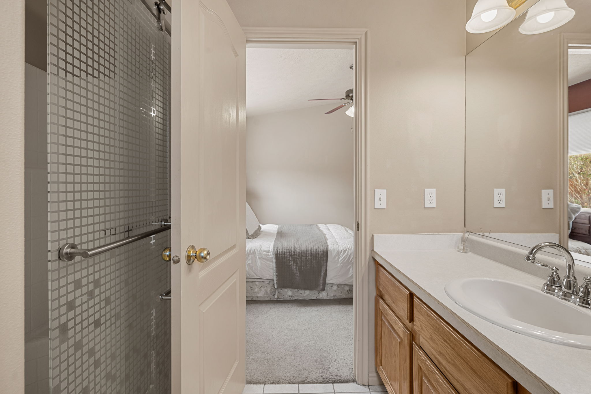 Bathroom featuring a patterned glass shower enclosure with a grab bar, a single vanity with a white countertop, wood-finish cabinetry, and a chrome faucet