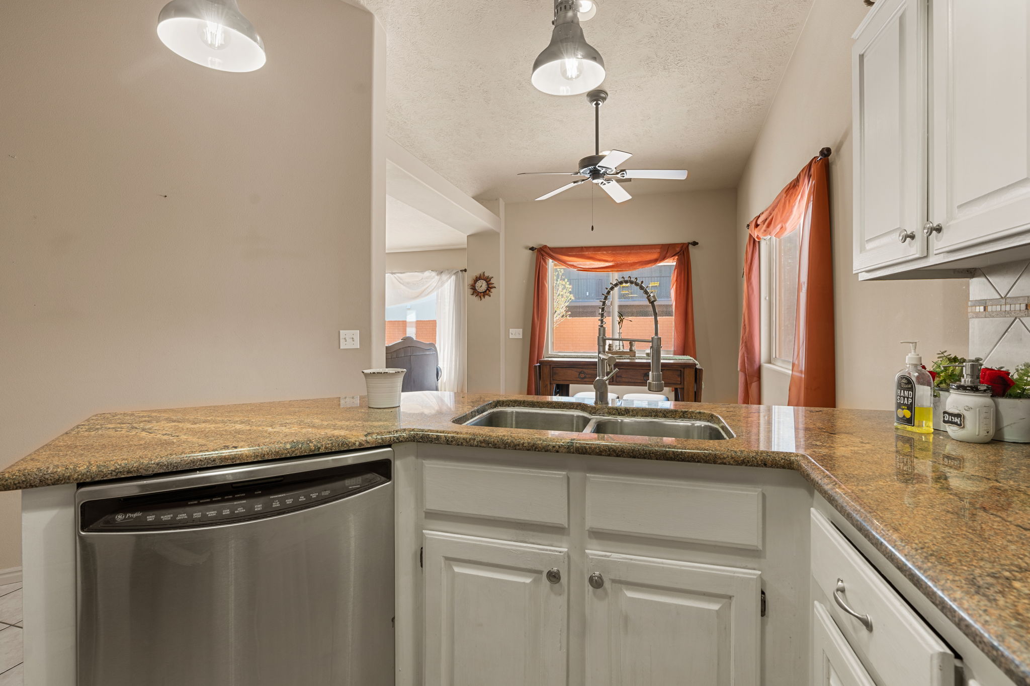 Kitchen featuring granite countertops, a double basin sink with a gooseneck faucet, white cabinetry, and stainless steel dishwasher