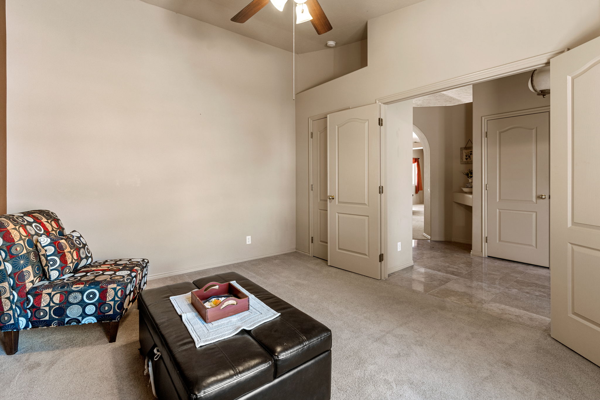 Carpeted room featuring a ceiling fan, arched doorways, a built-in wall niche, and tile flooring visible beyond the doorway