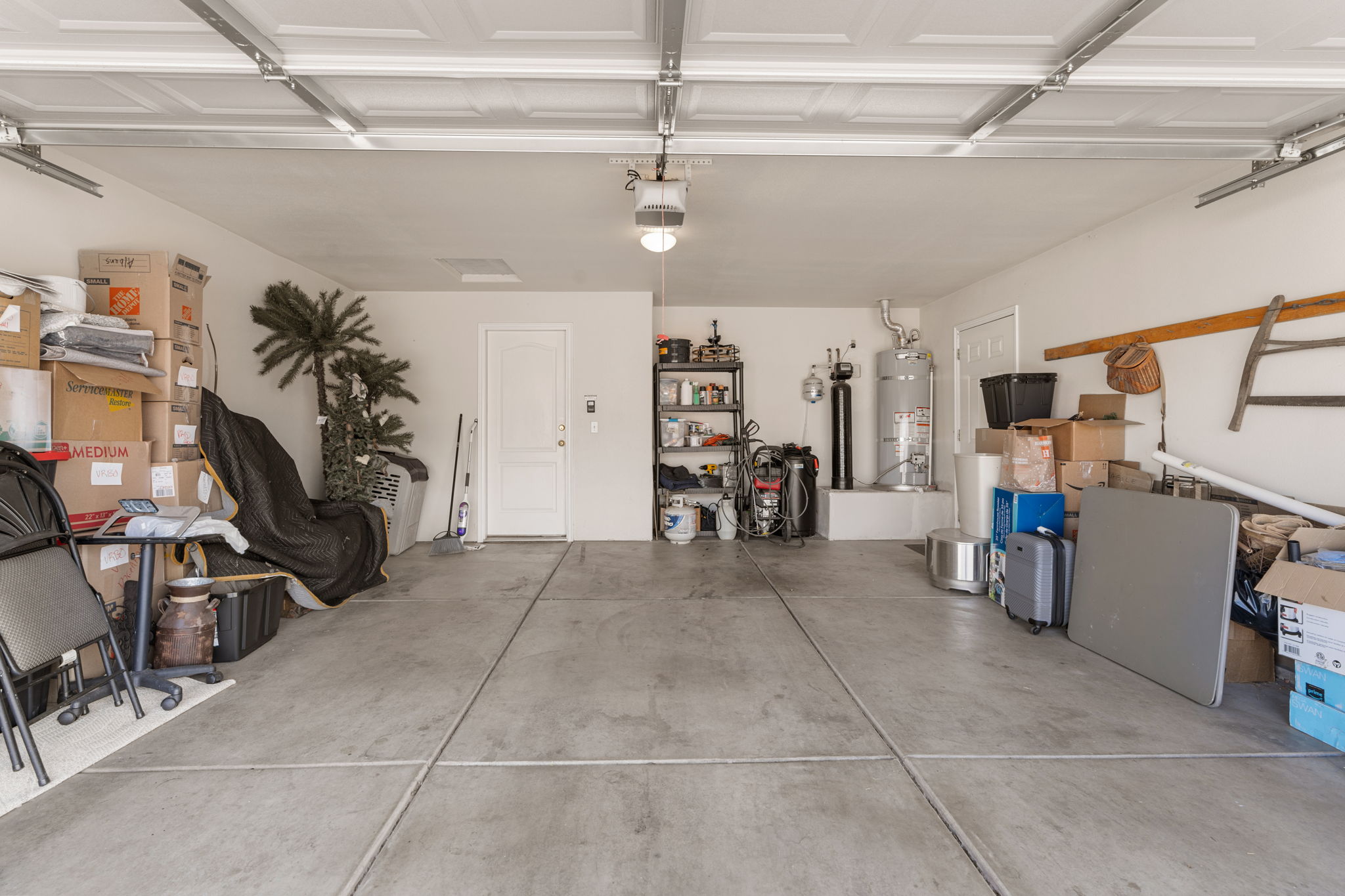 Spacious garage featuring a paneled overhead door, concrete flooring, interior access door, wall-mounted shelving, and a water heater