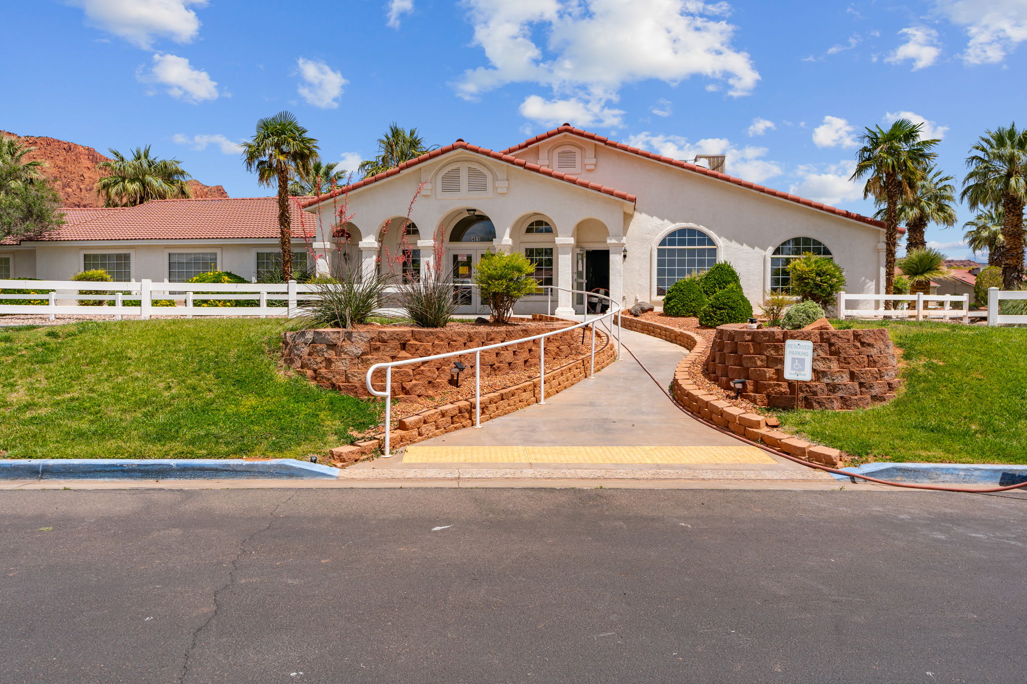 Spanish Colonial style building featuring a white stucco exterior, red tile roof, arched windows, and a paved entryway with handrails